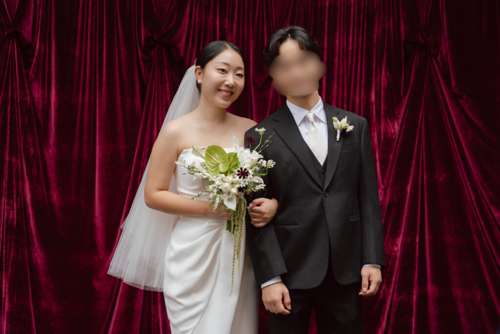 Bride and groom posing together at a red velvet photo booth on their wedding day